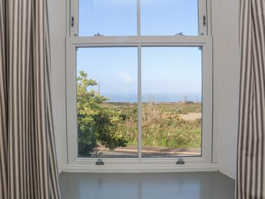 A window with striped curtains showing a view of bushes and sky at Bal View in St Just