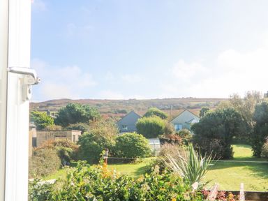 A garden with bushes and a lawn with houses and hills in the background at Bal View in St Just