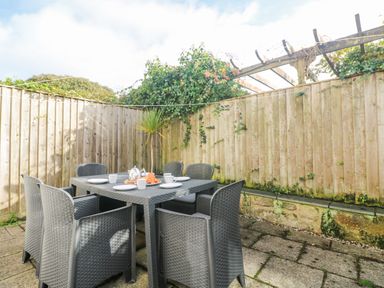 An outdoor patio with a table set for breakfast and six chairs surrounded by a wooden fence at Bal View in St Just