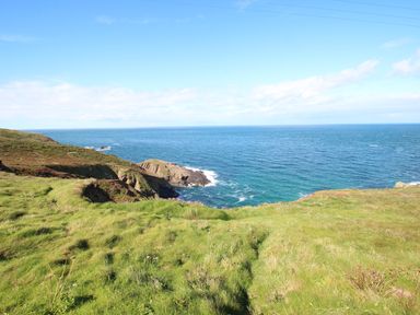 A coastal landscape with grass and rocky cliffs overlooking the ocean at Bal View in St Just
