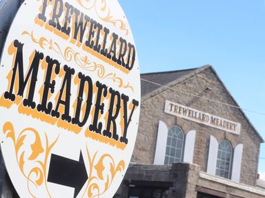 A stone building with arched windows and a sign reading Trewellard Meadery a circular sign with Trewellard Meadery and an arrow pointing right