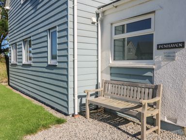A wooden bench outside a house with blue siding and white walls at Penhaven in Crackington Haven