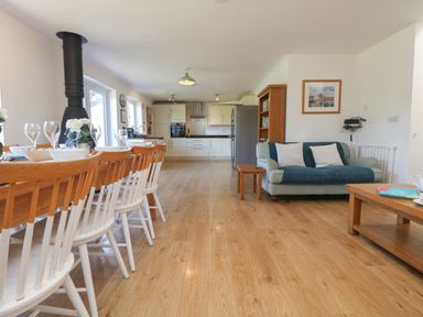 An open-plan kitchen and dining area with a wooden dining table and chairs a blue sofa and wooden coffee table at Penhaven in Crackington Haven