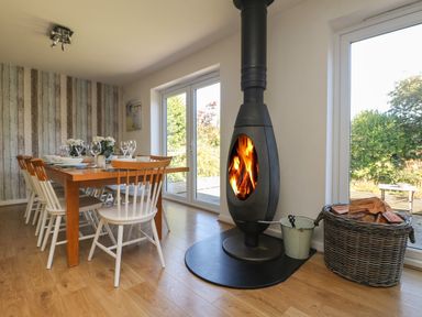 A dining room with a wooden table set with dishes and glasses next to a wood burning stove at Penhaven in Crackington Haven
