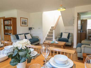 A dining table with white dishes and a flower pot in a living room with couches stairs and a bookshelf at Penhaven in Crackington Haven