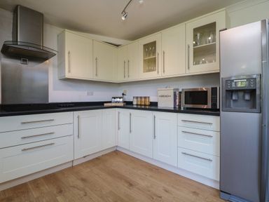 A kitchen with white cabinets black countertops a stainless steel refrigerator microwave and wooden floor at Penhaven in Crackington Haven