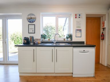 A kitchen with a black countertop white cabinets a sink dishwasher clock and a window with plants at Penhaven in Crackington Haven