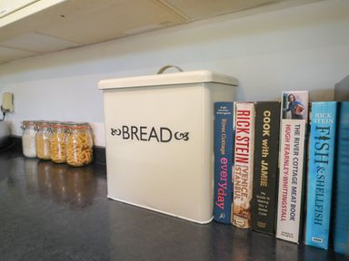A kitchen countertop with a bread box and several cookbooks next to glass jars containing rice and pasta at Penhaven in Crackington Haven