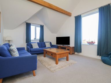 A living room with blue sofas a wooden coffee table a television and blue curtains at Penhaven in Crackington Haven