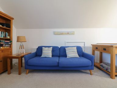 A blue sofa with two striped pillows between wooden side tables with a lamp on the left at Penhaven in Crackington Haven