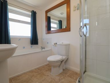A bathroom with a bathtub under a window with curtains a toilet a sink a large mirror and a shower with glass doors at Penhaven in Crackington Haven
