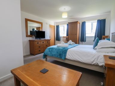 A bedroom with a bed covered by a blue throw and white linens two rolled towels on the bed wooden furniture including a dresser with a mirror wardrobe and a small table at Penhaven in Crackington Haven