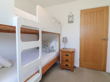 A bedroom with a wooden bunk bed two teddy bears on the bottom bed a wooden nightstand with a lamp and a wooden door at Penhaven in Crackington Haven
