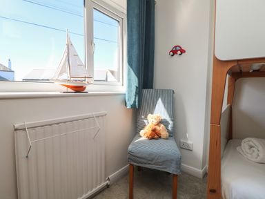 A small room with a chair holding two teddy bears a window with a model sailboat and part of a bunk bed at Penhaven in Crackington Haven