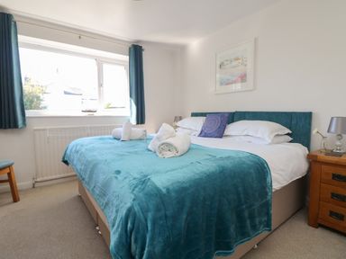 A bedroom with a large bed covered with teal blanket and pillows next to a wooden nightstand with a lamp at Penhaven in Crackington Haven