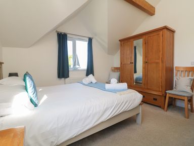 A bedroom with a bed, wooden wardrobe with mirror, two chairs with cushions, and a window with blue curtains at Penhaven in Crackington Haven