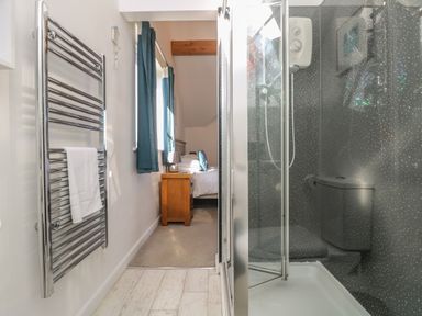 A bathroom with a shower and towel rack leading to a bedroom with a bedside table and bed at Penhaven in Crackington Haven