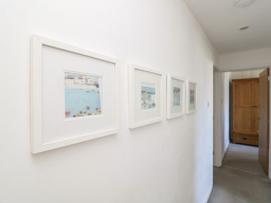 A hallway with four framed pictures on the wall and a wooden wardrobe in a room at the end at Penhaven in Crackington Haven