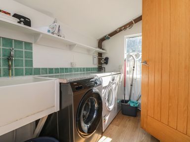A laundry room with a washing machine, dryer, sink, ironing board, and cleaning supplies at Penhaven in Crackington Haven