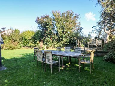 An outdoor garden with wooden table and chairs on grass and a wooden bench on a small deck at Penhaven in Crackington Haven