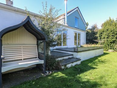 A garden with a covered wooden bench stone steps and a house with large windows at Penhaven in Crackington Haven