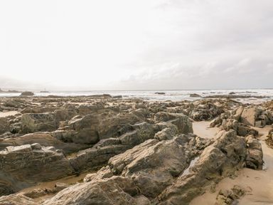 A rocky shoreline with scattered large rocks and sand meeting the ocean at Penhaven in Crackington Haven