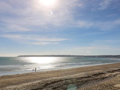 A beach with two people and a dog on the shore and a calm sea with a distant headland at Mackerel Sky in Marazion