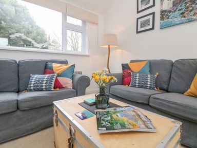 A living room with two gray sofas a wooden coffee table with magazines and a vase with yellow flowers at Mackerel Sky in Marazion