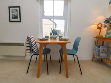 A dining area with a wooden table two blue chairs a table lamp and a window at Mackerel Sky in Marazion