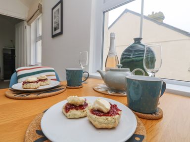 A table with scones topped with jam and cream two blue mugs a teapot a bottle and glasses by a window at Mackerel Sky in Marazion