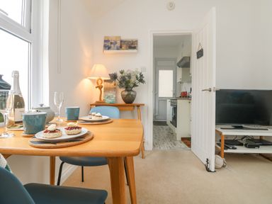 A dining area with a wooden table set with plates of scones and blue chairs next to a small table with a lamp and flowers in a vase at Mackerel Sky in Marazion
