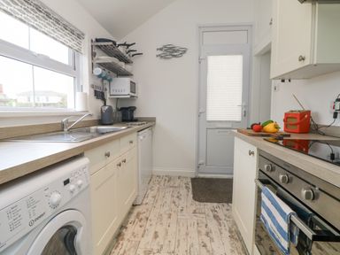 A kitchen with white cabinets a washing machine oven and a sink at Mackerel Sky in Marazion