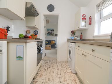 A kitchen with countertop appliances and fruit next to a doorway leading to a living room at Mackerel Sky in Marazion