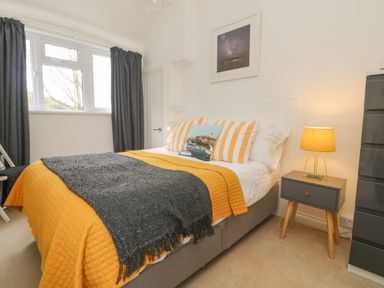 A bedroom with a bed with yellow and gray blankets a nightstand with a lamp and a dresser at Mackerel Sky in Marazion