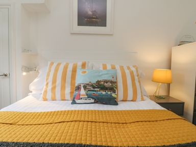 A bed with striped pillows and a decorative boat pillow a mustard quilt and a bedside table with a lamp and cabinets in a bedroom at Mackerel Sky in Marazion