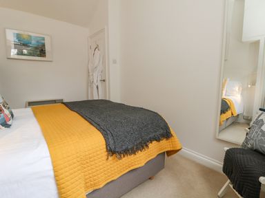 A bedroom with a bed covered by a yellow and gray blanket a chair with a cushion and a full-length mirror at Mackerel Sky in Marazion