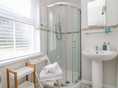 A bathroom with a glass shower enclosure a white pedestal sink a mirror a wooden chair with towels and a wooden storage rack at Mackerel Sky in Marazion