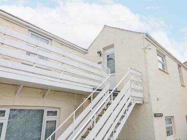 An exterior view of a beige building with white wooden stairs and railing leading to a second floor door at Mackerel Sky in Marazion
