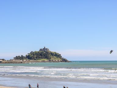 A beach with people walking near the shore and a castle on a hill by the sea at Mackerel Sky in Marazion