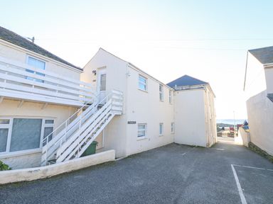 A white building with stairs and a parking area near the sea at Mackerel Sky in Marazion