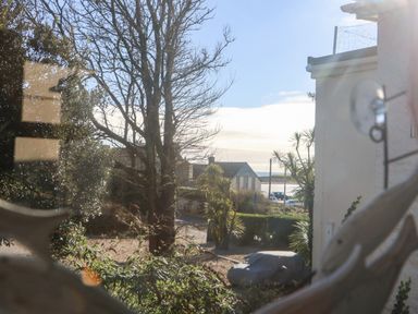 View through a window showing trees a covered car a small building and a body of water at Mackerel Sky in Marazion