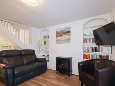 A living room with a black sofa black armchair bookshelf and a wall-mounted TV at Alma House 2 in Perranporth