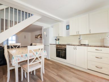 A kitchen and dining area with white cabinets a dining table with chairs and a staircase at Alma House 2 in Perranporth