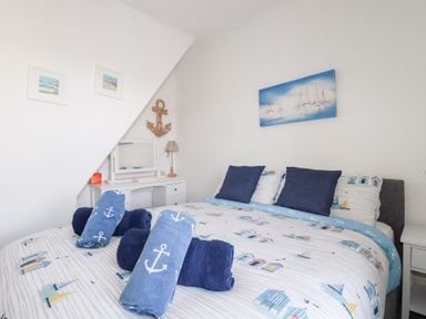 A bedroom with a bed and rolled towels on a nautical themed bedspread at Alma House 2 in Perranporth