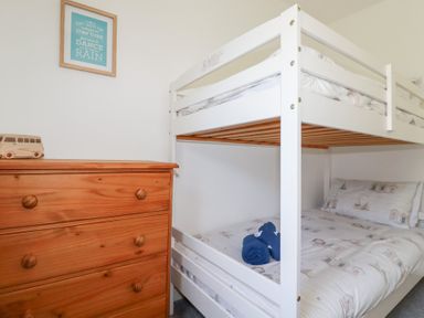 A bedroom with a wooden chest of drawers and a white bunk bed with blue towels on the lower bed at Alma House 2 in Perranporth