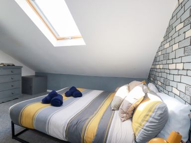 A bedroom with a bed with striped bedding and multiple pillows under a skylight at Alma House 2 in Perranporth