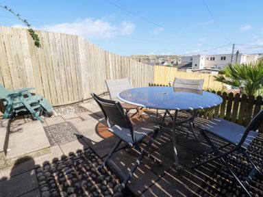A patio area with a round glass table and four chairs surrounded by wooden fences at Alma House 2 in Perranporth