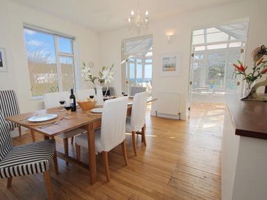 A dining area with a wooden table and chairs set with plates glasses and flowers at Porthcurno Bay View in Porthcurno