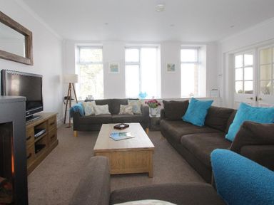 A living room with brown sofas blue cushions a wooden coffee table and a television at Porthcurno Bay View in Porthcurno