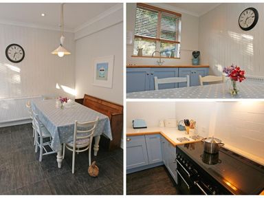 A kitchen and dining area with a table covered by a blue polka dot tablecloth surrounded by chairs and a bench a sink below a window with blinds and blue cabinets and a stove with a pot on it at Porthcurno Bay View in Porthcurno